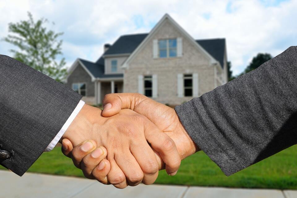 Realtor and seller shaking hands in front of sold home